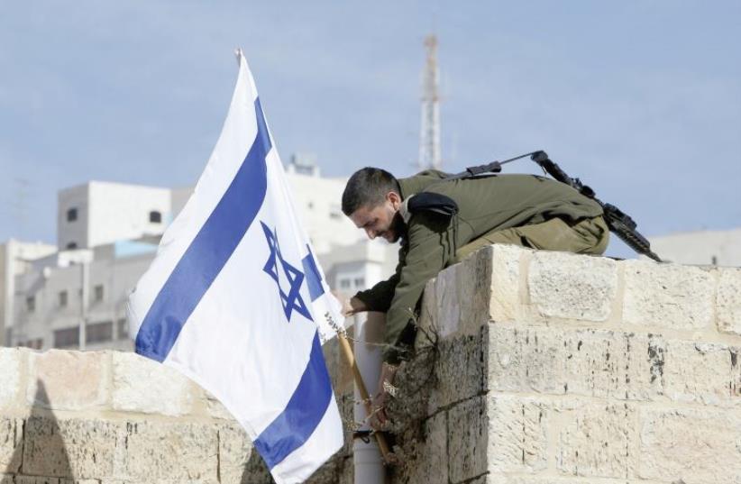 A SOLDIER holds a flag atop a house in Hebron. (photo credit: REUTERS)