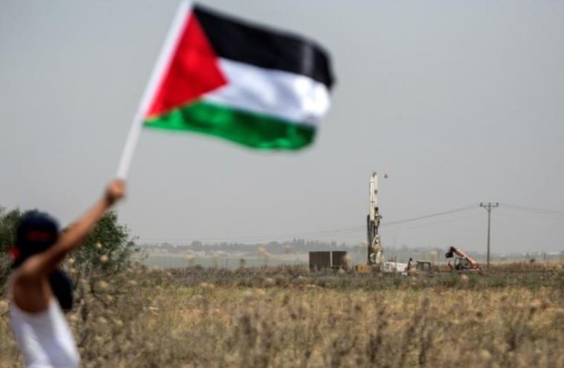 A Palestinian youth waves the national flag as the IDF digs in search of smuggling tunnels at the border east of Gaza City (photo credit: AFP PHOTO)