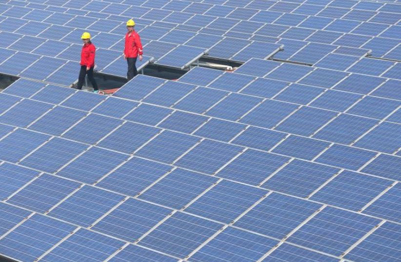 Workers walk past solar panels in Jimo, Shandong Province, China (photo credit: REUTERS)