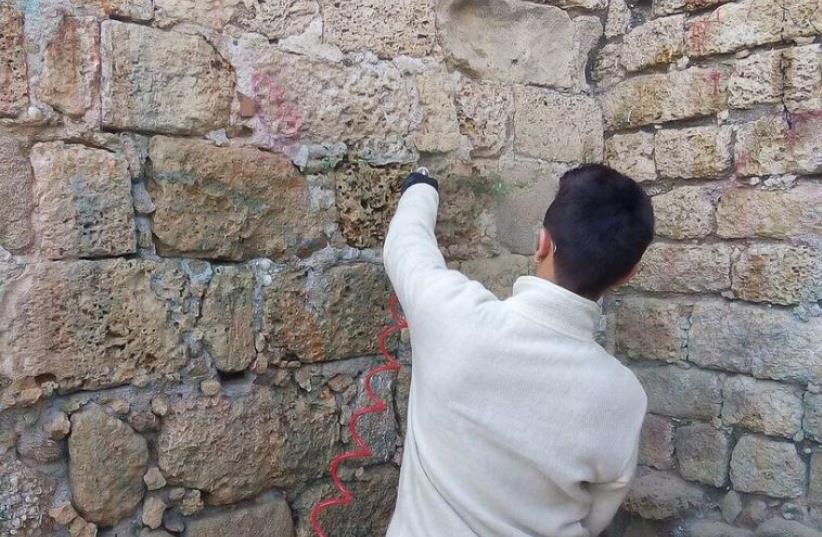 One of the teenagers responsible for dousing the wall in paint works with IAA archeologists to restore it. (photo credit: ARIEL INBAR/IAA)