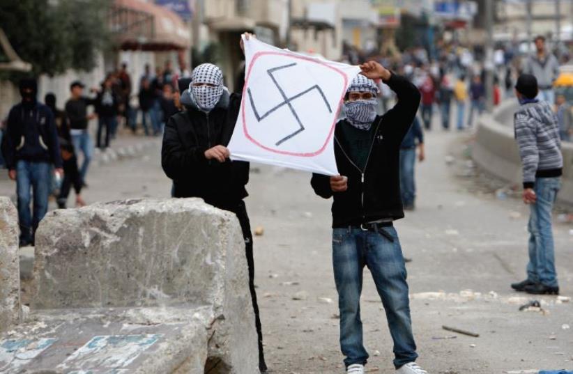 Palestinians hold a sign depicting a swastika during clashes at Qalandiya checkpoint near the West Bank city of Ramallah in 2010. (photo credit: REUTERS)