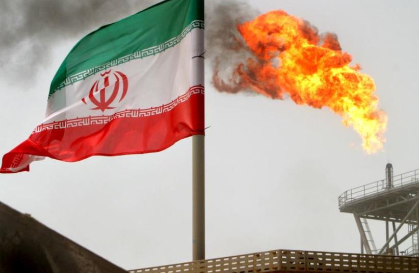 A gas flare on an oil production platform in the Soroush oil fields is seen alongside an Iranian flag in the Gulf  (photo credit: RAHEB HOMAVANDI/REUTERS)