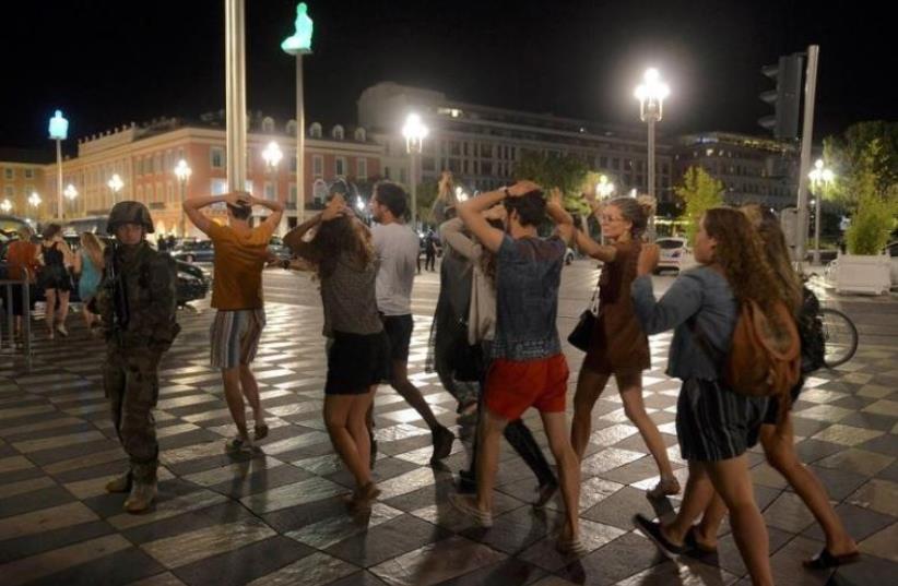 People cross the street with their hands on thier heads as a French soldier secures the area July 15, 2016 after at least 60 people were killed along the Promenade des Anglais in Nice, France, when a truck ran into a crowd celebrating the Bastille Day national holiday July 14.  (photo credit: REUTERS/JEAN-PIERRE AMET)