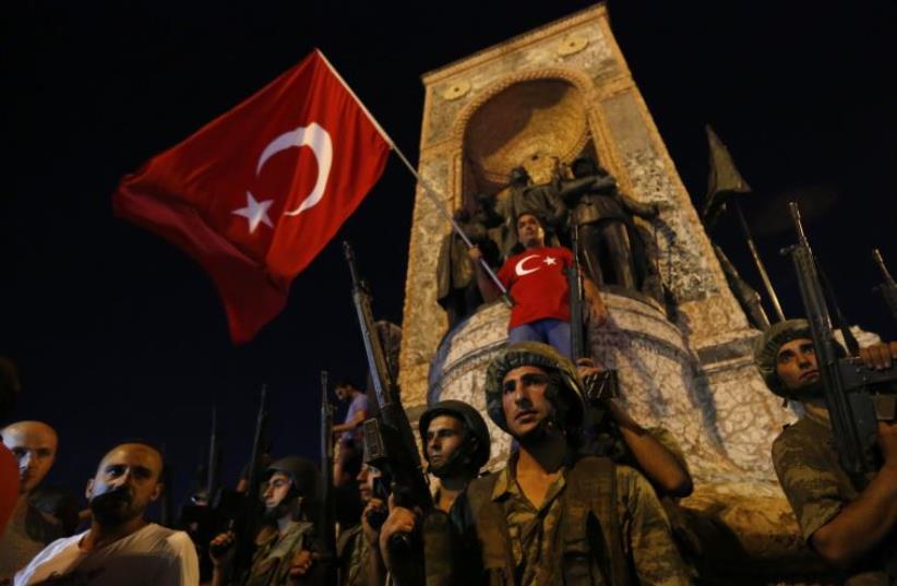 Turkish military stand guard near the the Taksim Square as people wave with Turkish flags in Istanbul, Turkey, July 16, 2016 (photo credit: REUTERS)