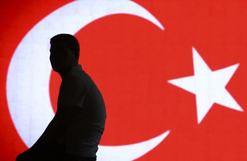 Man sits in front of Turkish flag hours after coup in Turkey thwarted (photo credit: REUTERS)