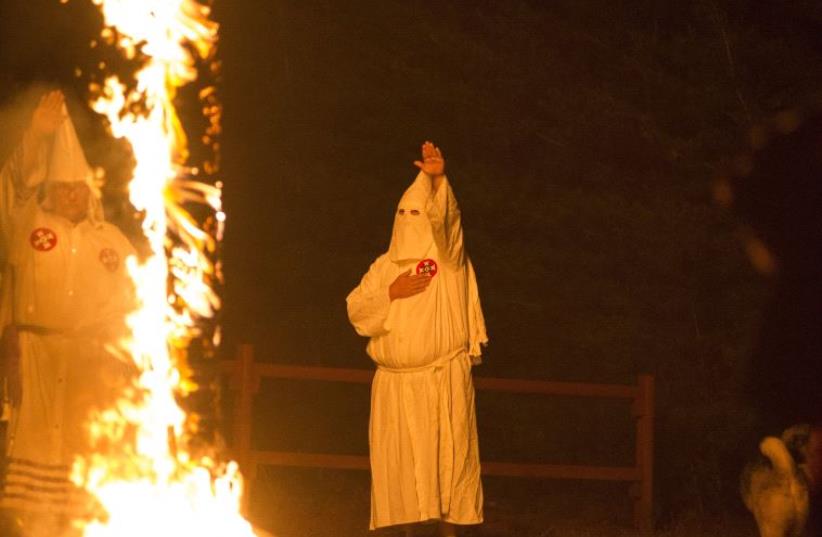 A member of the Ku Klux Klan salutes a lit cross during a cross lighting ceremony. (photo credit: REUTERS)