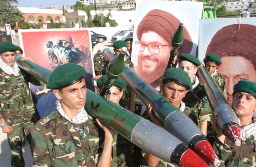 Hezbollah members carry mock rockets next to a poster of the group's leader Sayyed Hassan Nasrallah [FIle] (photo credit: REUTERS)