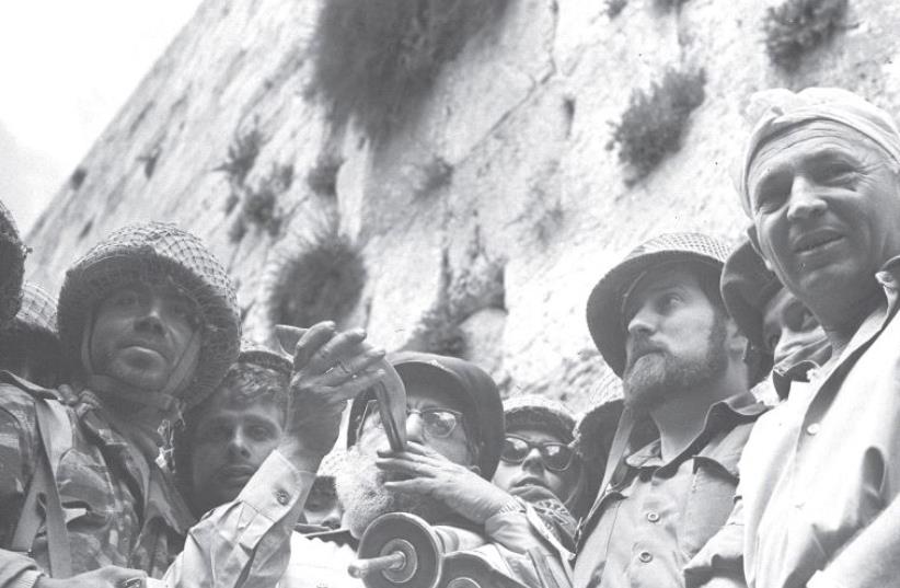IDF CHIEF RABBI Shlomo Goren blows a shofar while he clutches a Torah scroll at the Western Wall on the day Jerusalem was reunified in June 1967 (photo credit: GPO)