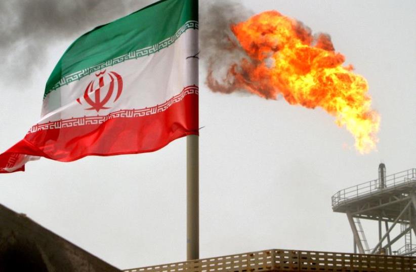 A gas flare on an oil production platform in the Soroush oil fields is seen alongside an Iranian flag in the Persian Gulf, Iran, July 25, 2005. (photo credit: REUTERS)