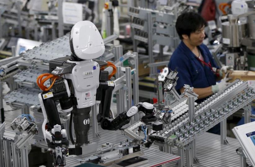 A humanoid robot works side by side with employees in the assembly line at a factor (photo credit: REUTERS)