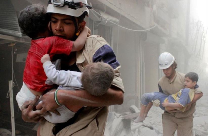 Members of the Civil Defence rescue children after what activists said was an air strike by forces loyal to Syria's President Bashar al-Assad in al-Shaar neighbourhood of Aleppo, Syria June 2, 2014 (photo credit: REUTERS)