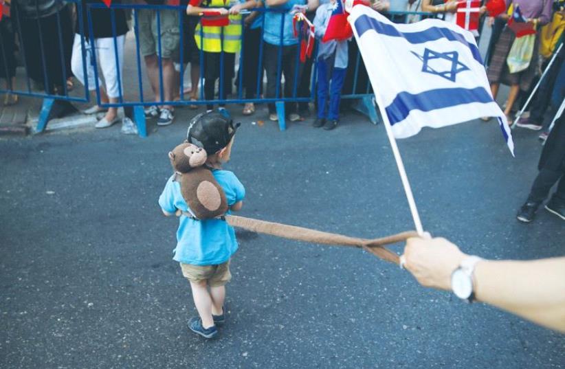 A young boy on a leash while someone holds an Israeli flag (photo credit: REUTERS)