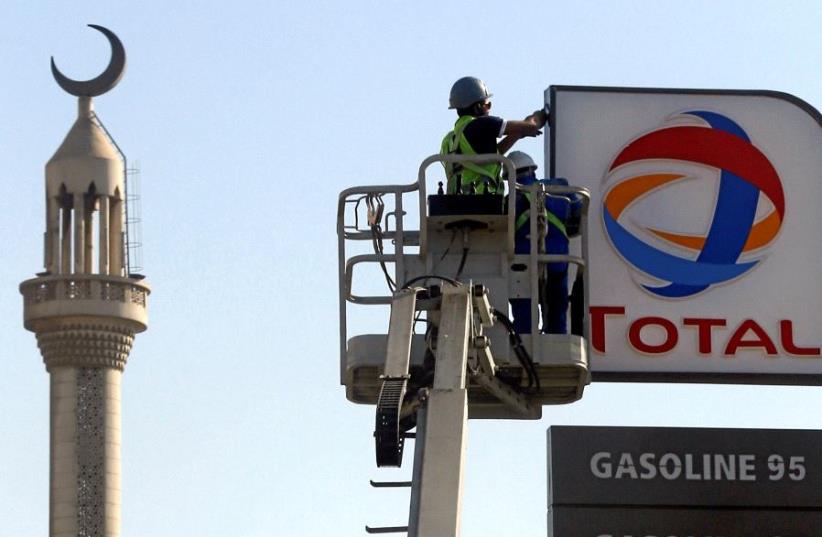 FILE PHOTO: Workers fix a sign for oil giant Total at a petrol station in Cairo, Egypt, October 13, 2016.  (photo credit: REUTERS)