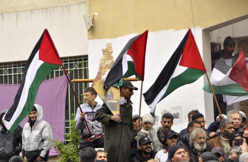 Palestinian residents of the Yarmouk refugee camp in the Damascus district of Syria wave their national flags as they take part in a protest expressing their will to stay inside the camp. (photo credit: REUTERS)