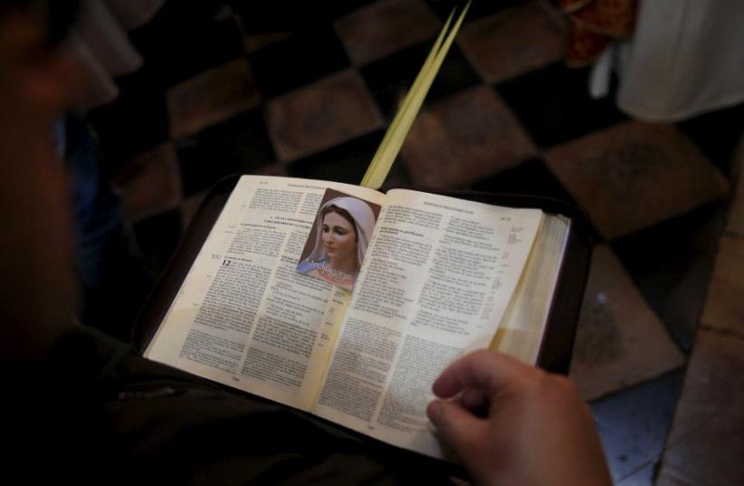 A worshipper holds an opened Bible during a Palm Sunday procession at the Church of the Holy Sepulchre in Jerusalem's Old City. (photo credit: REUTERS)