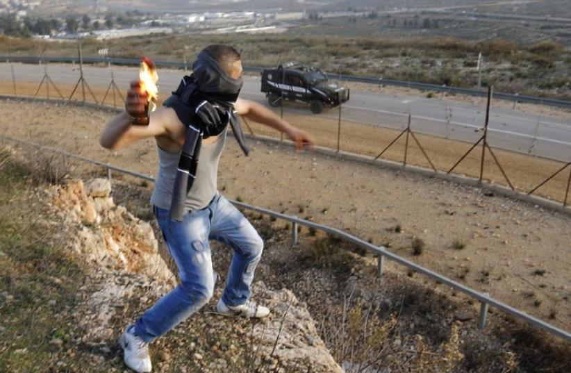 WHO IS paying him? A Palestinian throws a molotov cocktail at an Israeli jeep (photo credit: REUTERS)