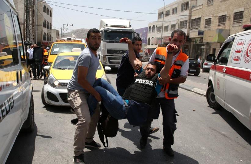 A wounded Palestinian reporter is carried by a medic and civilians on May 18, 2017 near the Hawara military checkpoint. (photo credit: JAAFAR ASHTIYEH / AFP)
