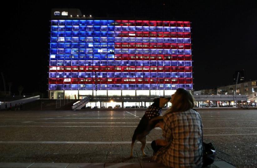 A woman plays with her dog as the municipality building is lit in the colours of the American flag on the first day of U.S. President Donald Trump's visit in Israel, in Tel Aviv, Israel May 22, 2017. (photo credit: REUTERS/CORINNA KERN)