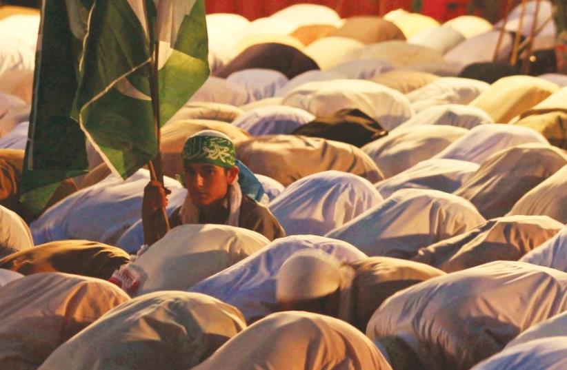 A SUPPORTER of Jamaat-e-Islami, a Pakistani religion-based political party, holds the national flag while sitting among others offering evening prayers in Islamabad, Pakistan. (photo credit: REUTERS)