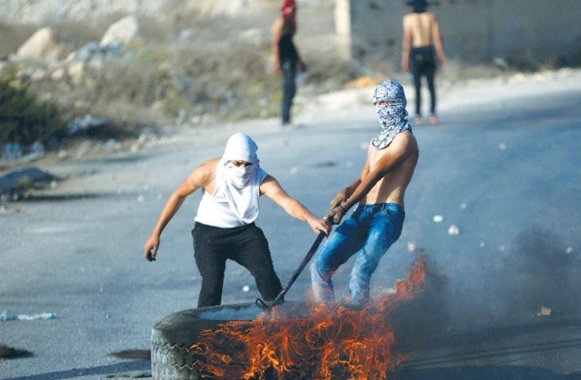 PALESTINIAN PROTESTERS drag a burning tire during a protest in a-Ram, northeast of Jerusalem. (photo credit: MOHAMAD TOROKMAN/REUTERS)