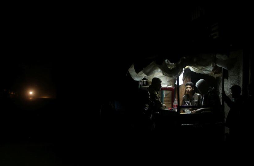 A Palestinian man sells falafel in a makeshift shop lit with a lamp powered by a battery during a power cut in Beit Lahiya in the northern Gaza Strip January 11, 2017. Picture taken January 11, 2017.  (photo credit: REUTERS/MOHAMMED SALEM)