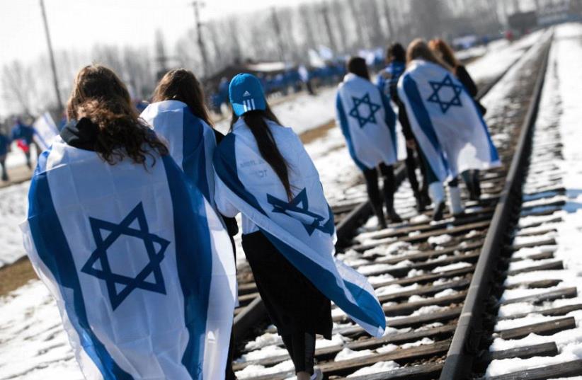 People wear Israeli flags around their shoulders as they walk on the railroad tracks inside the former Nazi death camp of Birkenau (Auschwitz II) in Oswiecim-Brzezinka, southern Poland April 8, 2013. (photo credit: REUTERS/JAKUB OCIEPA/AGENCJA GAZETA)
