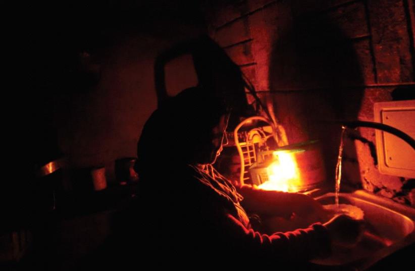 A Palestinian woman washes by candlelight during a power cut in the kitchen of her home in Beit Lahiya in the northern Gaza Strip (photo credit: REUTERS)