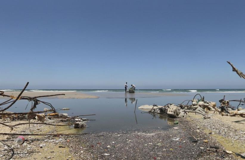 Palestinian fishermen are reflected in wastewater as they prepare their boat on a beach in the central Gaza Strip June 26, 2014. (photo credit: REUTERS/MOHAMMED SALEM)