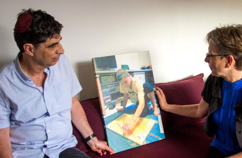 Simha and Leah Goldin with a   photo of Hadar doing one of the activities he loved - painting - his last piece before he was killed. (photo credit: LAURA BEN-DAVID)