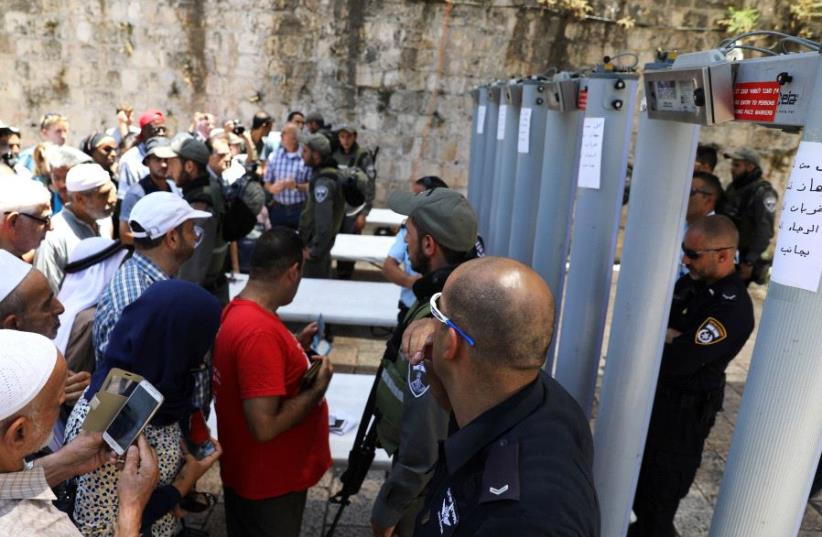 Palestinians stand in front of Israeli police officers and newly installed metal detectors at an entrance to the  Temple Mount, in Jerusalem's Old City July 16, 2017. (photo credit: REUTERS)