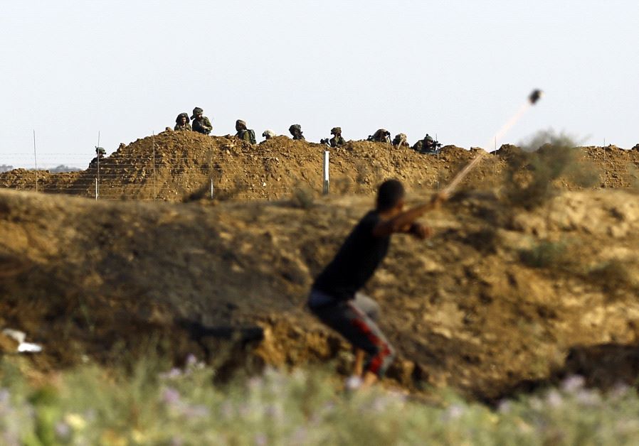 A Palestinian protester uses a sling to hurl a stone towards Israeli troops during clashes with Israeli security forces near the border fence east of Jabalia refugee camp on July 21, 2017  (photo credit: MOHAMMED ABED / AFP)