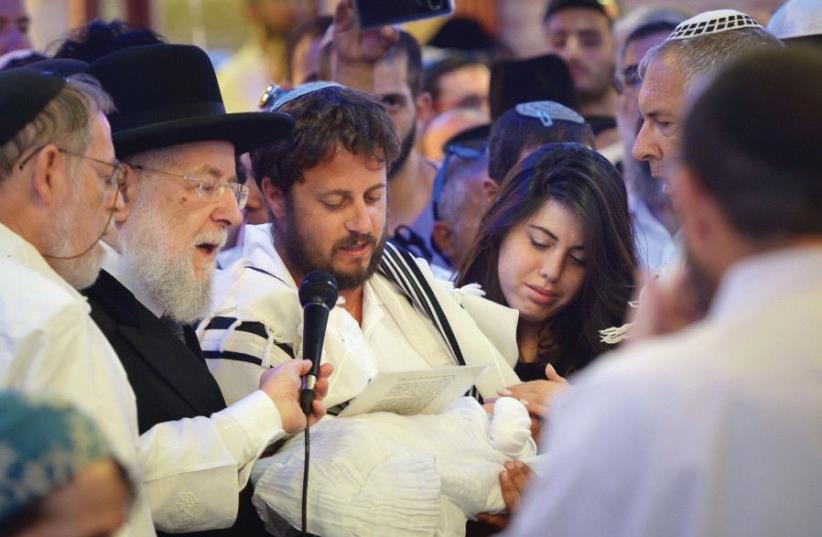 EIGHT-DAY-OLD Ari Yosef Salomon is held by his father, Shmuel, as the infant’s mother, Chen, looks on and Rabbi Israel Meir Lau (second left) officiates at the brit in El’ad, July 27, 2017. (photo credit: FLASH90)