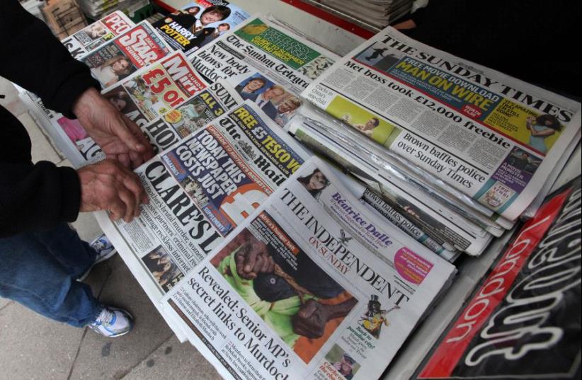 A man buys a Sunday newspaper at a news stand in London July 17, 2011. (photo credit: REUTERS/SUZANNE PLUNKETT)