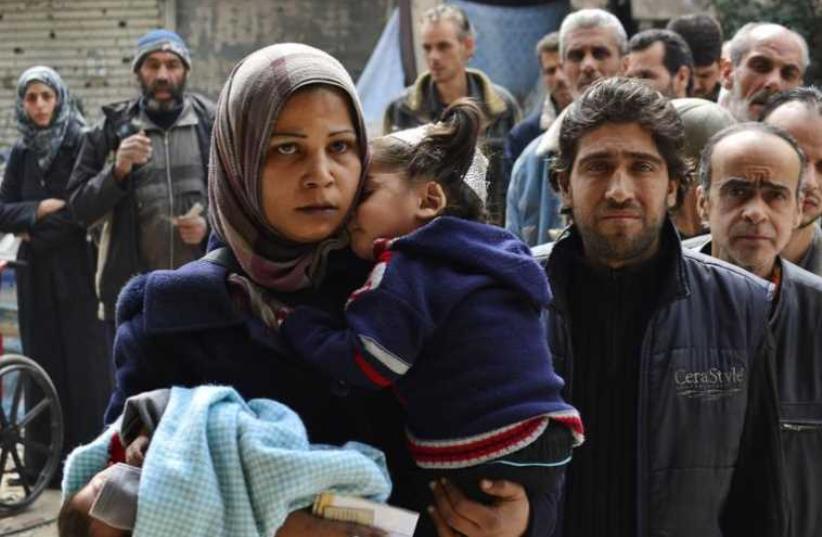 Residents queue up to receive humanitarian aid at the Palestinian refugee camp of Yarmouk (photo credit: REUTERS)