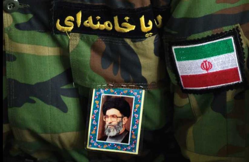 A WORSHIPPER pastes a portrait of Iran’s Supreme Leader Ayatollah Ali Khamenei, a flag and a Persian script that reads, ‘Hey Khamenei’ on a Revolutionary Guard uniform (photo credit: REUTERS)