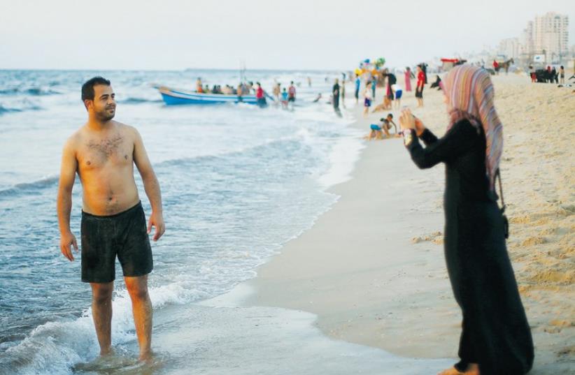 A PALESTINIAN woman takes a photograph of her husband on a mobile phone at the beach in Gaza City (photo credit: REUTERS)