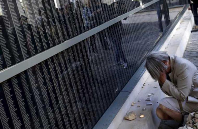 A woman prays in front of a wall bearing the names of victims during Holocaust Memorial day at Budapest's Holocaust Memorial Center (photo credit: REUTERS)