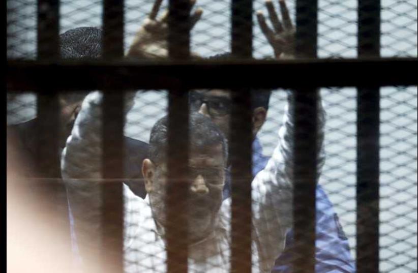 Ousted Egyptian President Mohamed Morsi gestures after his trial behind bars at a court in the outskirts of Cairo (photo credit: REUTERS)