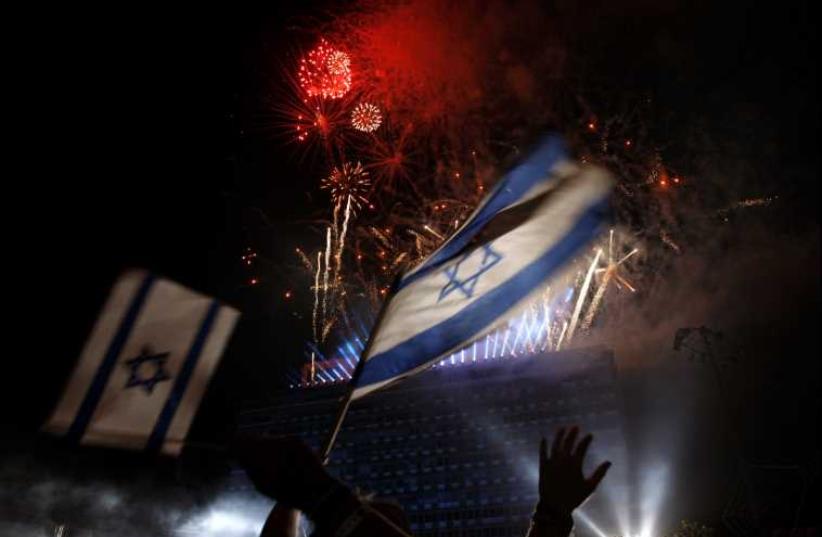 Israelis wave national flags as they watch fireworks during celebrations marking Israel's Independence Day in Tel Aviv  (photo credit: REUTERS)