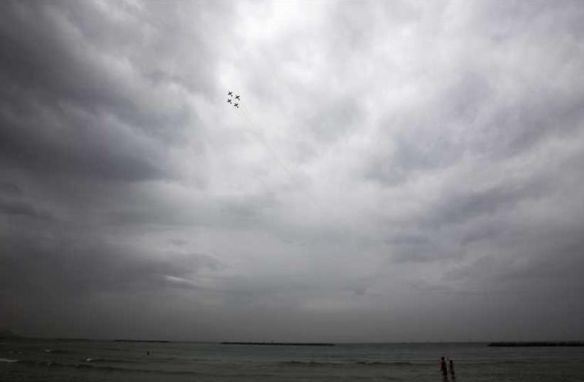 People walk on the beach as Israeli Air Force planes fly above during an aerial show as part of celebrations for Israel's Independence Day, in Tel Aviv May 6, 2014 (photo credit: REUTERS)