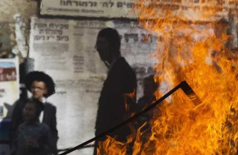 Ultra-Orthodox Jewish bystanders are seen through a heat mirage from a fire set by demonstrators during a protest in Jerusalem's Mea Shearim neighborhood (photo credit: REUTERS)