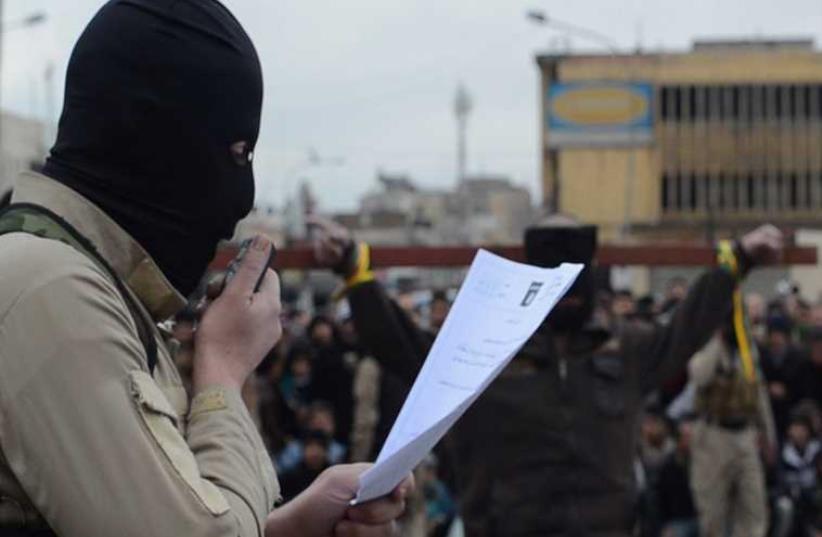 A masked Islamic State militant reads the charges of two men tied to a cross (photo credit: SCREENGRAB/JUSTPASTE.IT)