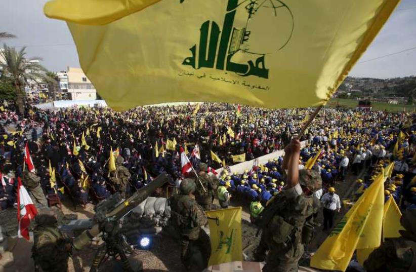 A Hezbollah member carries a Hezbollah flag while leader Hassan Nasrallah talks on a screen during a televised speech at a festival celebrating 'Resistance and Liberation Day' (photo credit: REUTERS)