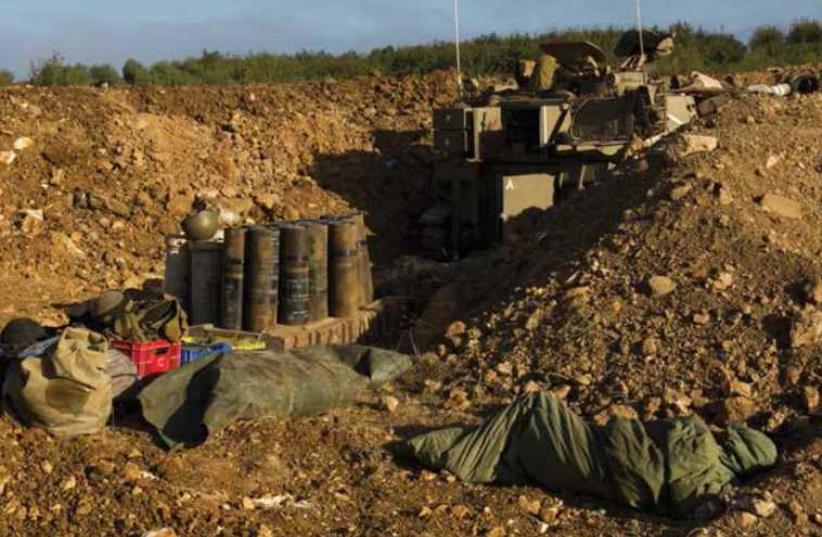 A soldier sleeps in a trench next to an armored vehicle on the Golan Heights. (photo credit: REUTERS)