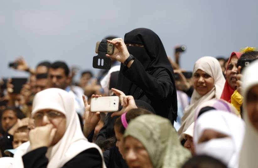 A Palestinian woman takes pictures as Palestinian Hamas security forces perform during their military training graduation ceremony in Gaza City (photo credit: MOHAMMED ABED / AFP)