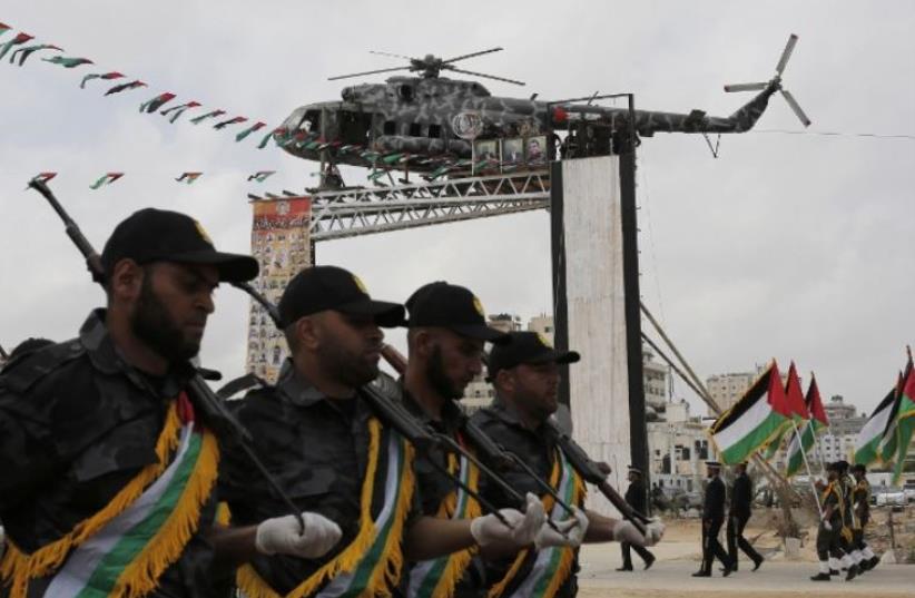 Hamas security forces march during a military review near a recently installed statue of a renovated helicopter belonging to late Palestinian leader Yasser Arafat (photo credit: MOHAMMED ABED / AFP)