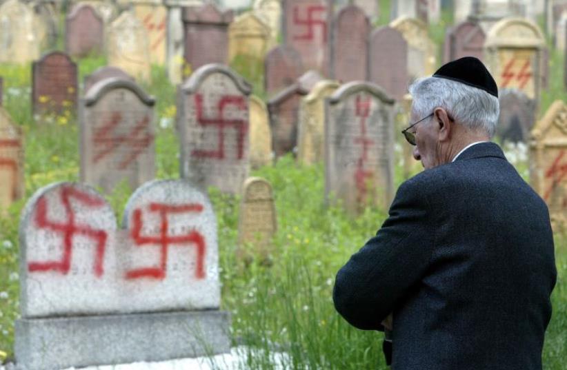 A Jewish man stands near some of the 127 graves desecrated by vandals with Nazi swastikas and anti-semitic slogans in the Jewish cemetery of Herrlisheim  (photo credit: REUTERS)