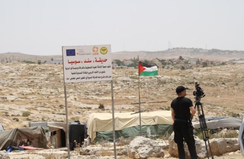 The tents of the illegal Palestinian village of Sussiya, with the Jewish settlement in the background. An EU logo is on a sign not far from the Palestinian flag (photo credit: TOVAH LAZAROFF)