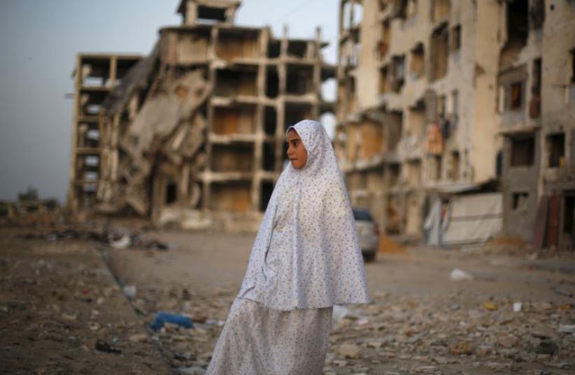 A Palestinian girl stands near residential buildings that witnesses said were heavily damaged by Israeli shelling during a 50-day war last summer (photo credit: REUTERS)