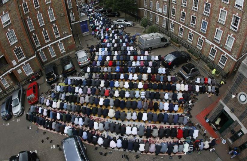 Muslims attend Friday prayers during the second day of Ramadan, in the courtyard of a housing estate next to the small BBC community centre and mosque (R) in east London, Britain June 19, 2015.  (photo credit: REUTERS)